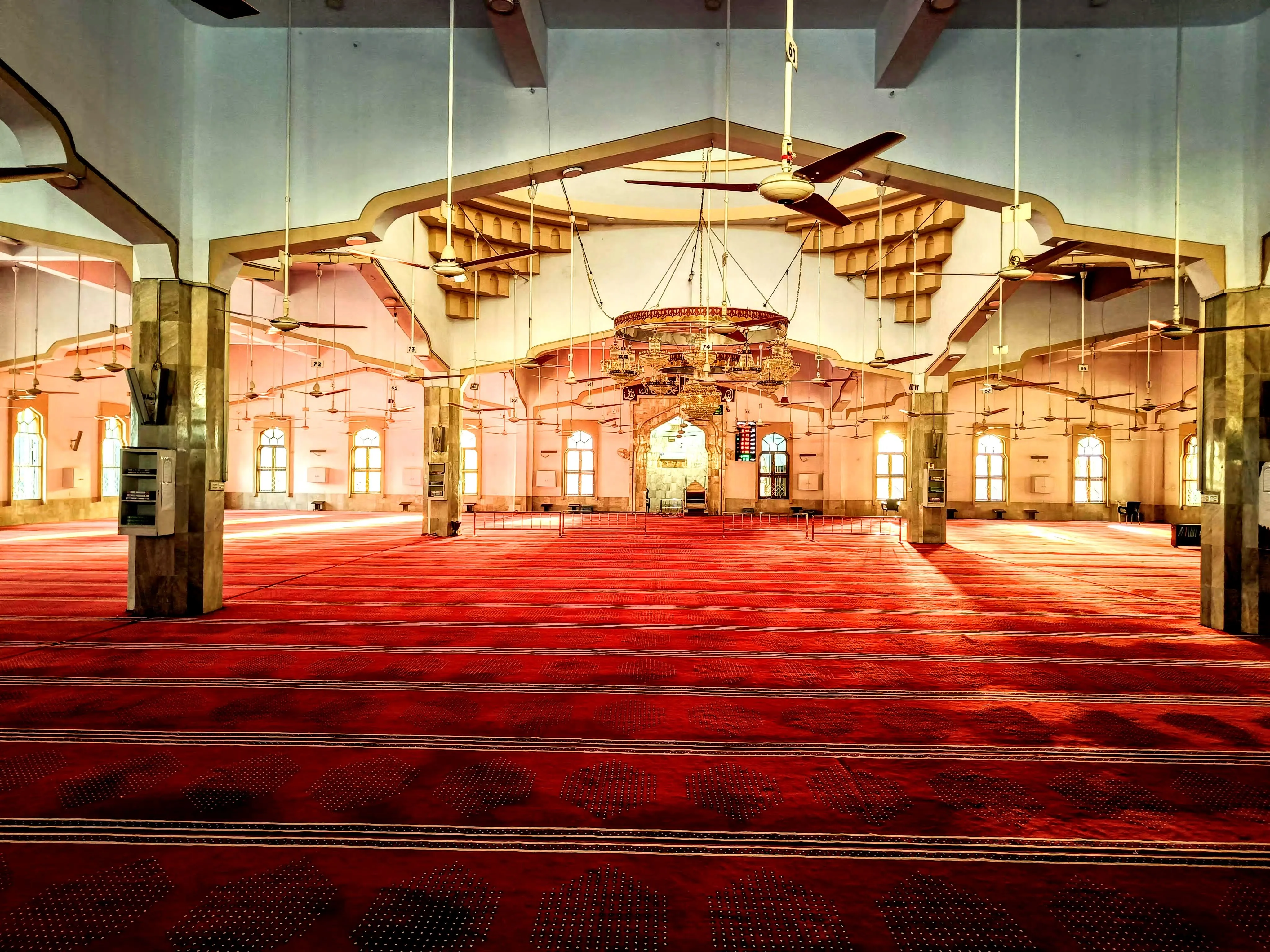 Main prayer hall of Bait ul Mukarram — red carpet stretching toward the mihrab, arched windows on both sides