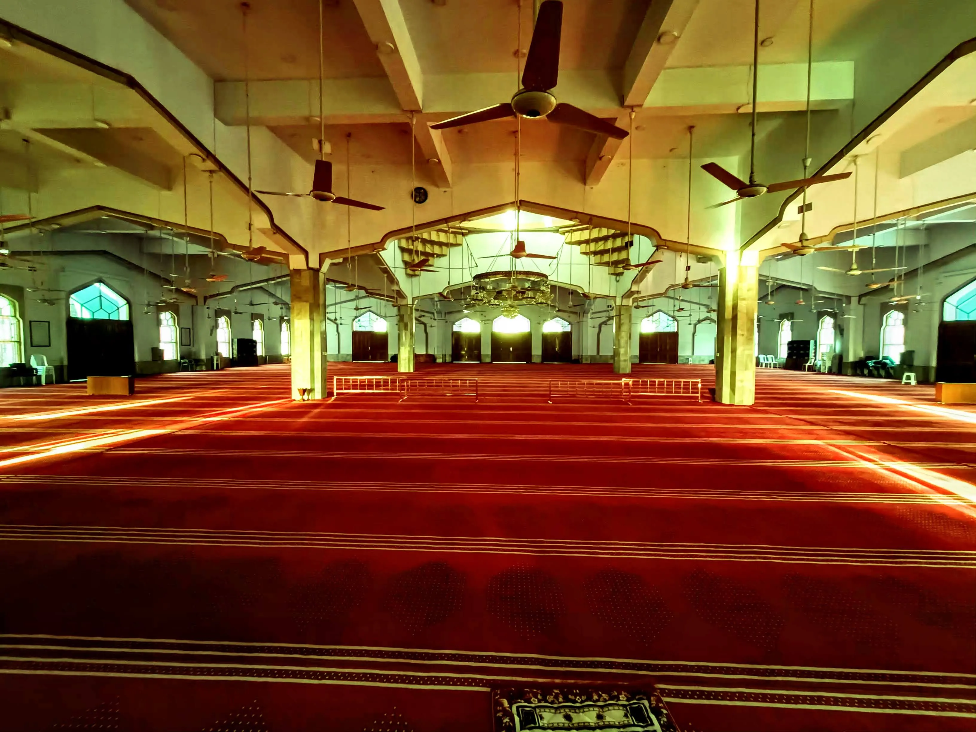 The main prayer hall of Jamia Masjid Bait ul Mukarram — red carpet, chandelier, and arched ornamental ceiling looking toward the mihrab