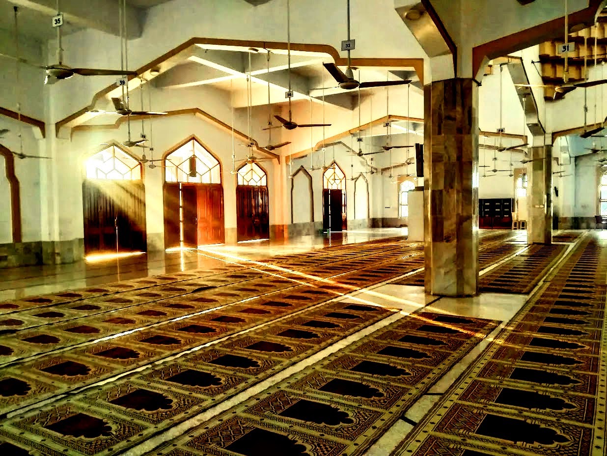 Inside the prayer hall of Bait ul Mukarram — morning light streaming through arched windows onto the carpet