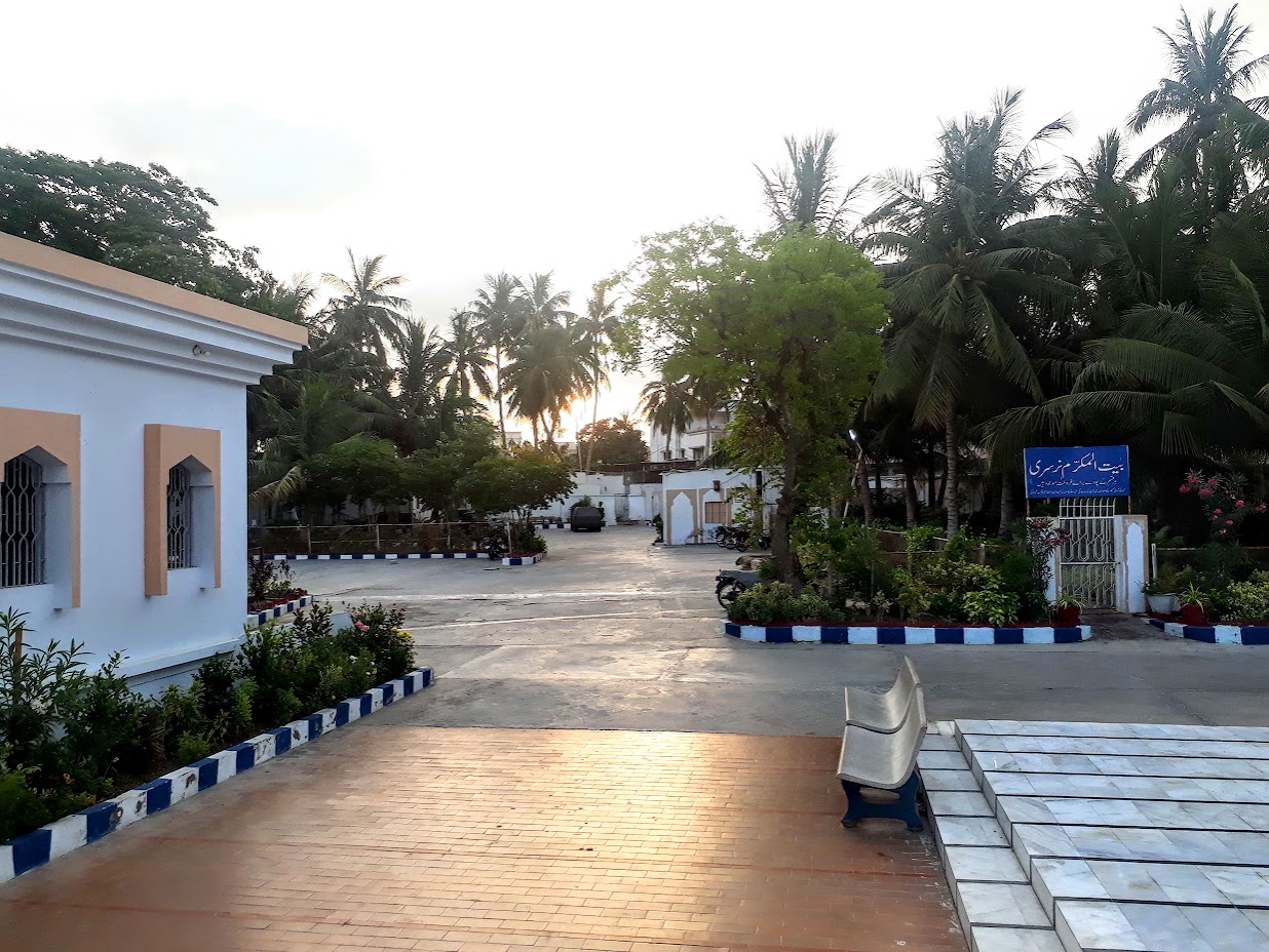 The Bait ul Mukarram nursery path at sunrise — بیت المکرم نرسری sign, potted plants, coconut palms