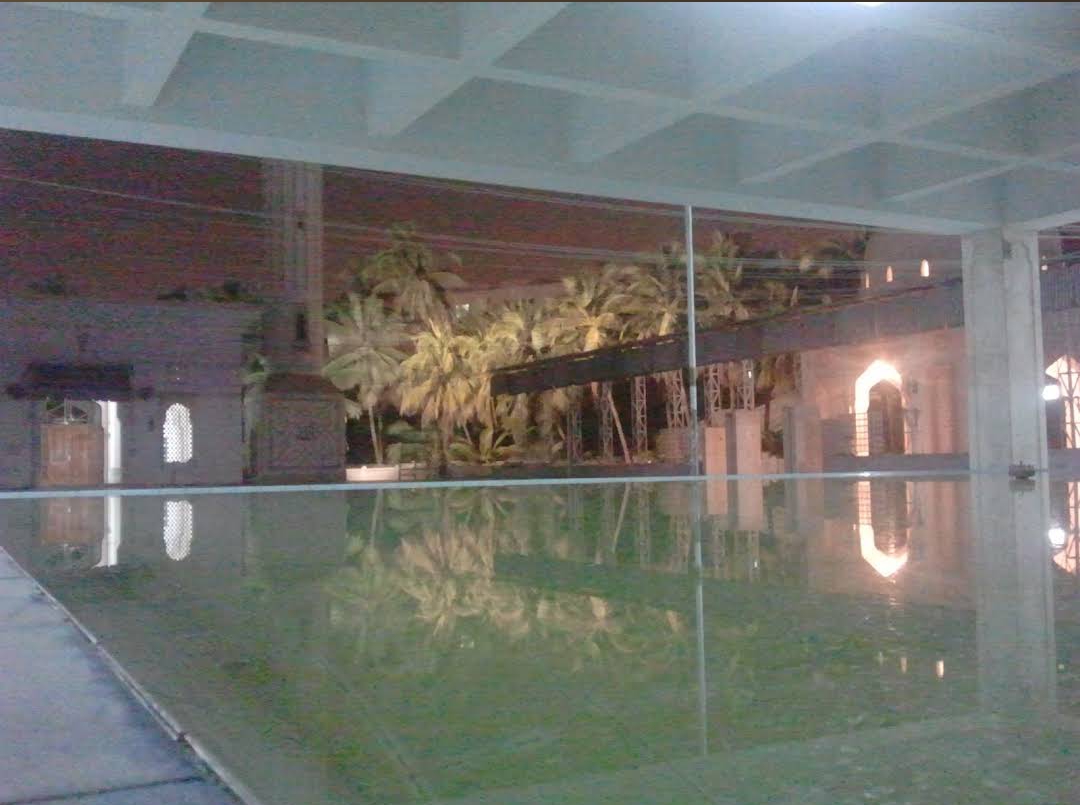The original wuzu pool at Bait ul Mukarram — a large open water basin reflecting the palm trees and arched walkway, now dismantled