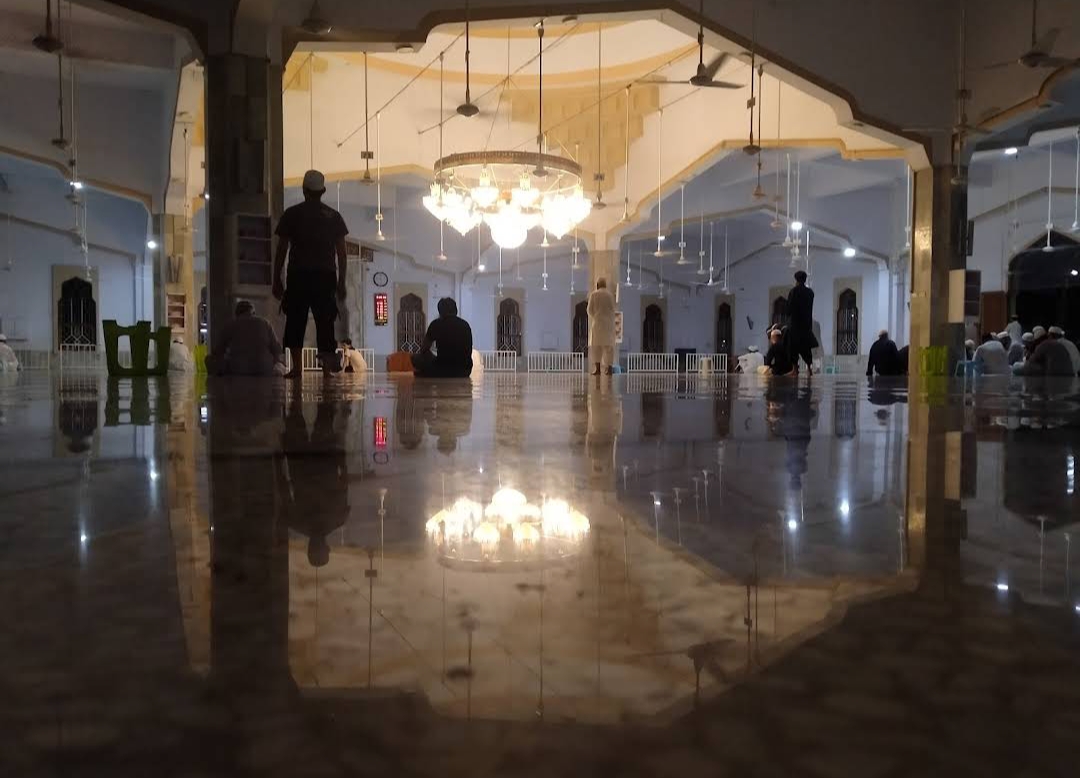 Interior of Bait ul Mukarram — marble floor with geometric inlay, chandeliers, arched windows, daytime